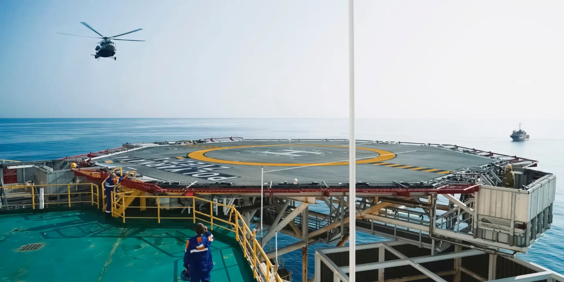 Offshore helideck with crew on station as a helicopter approaches the installation.