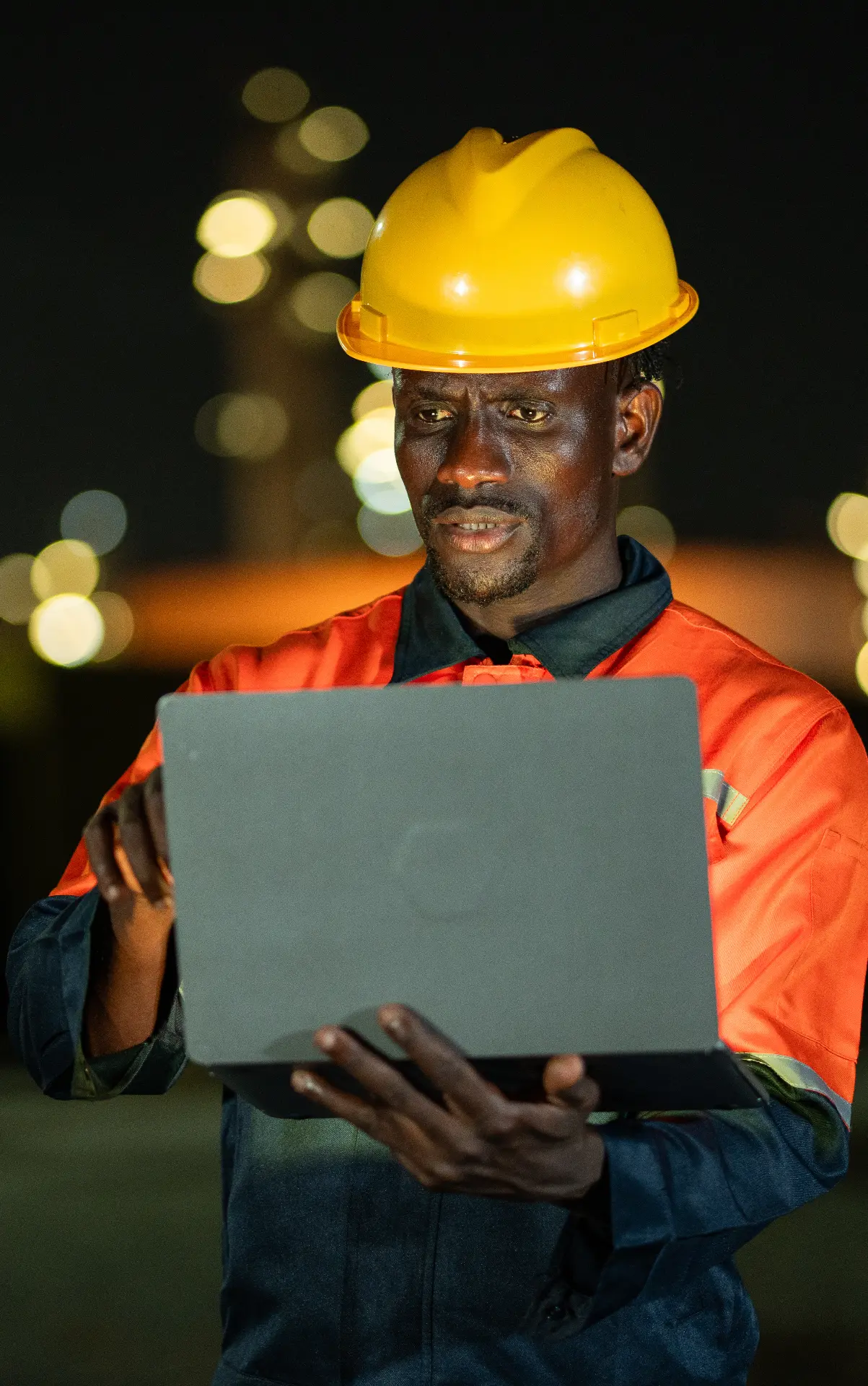 Engineer working on a laptop at an illuminated industrial plant at night.