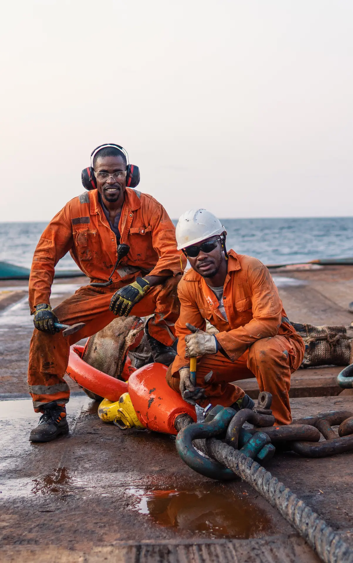 Offshore crew in protective equipment working mooring chains and buoy equipment on deck.