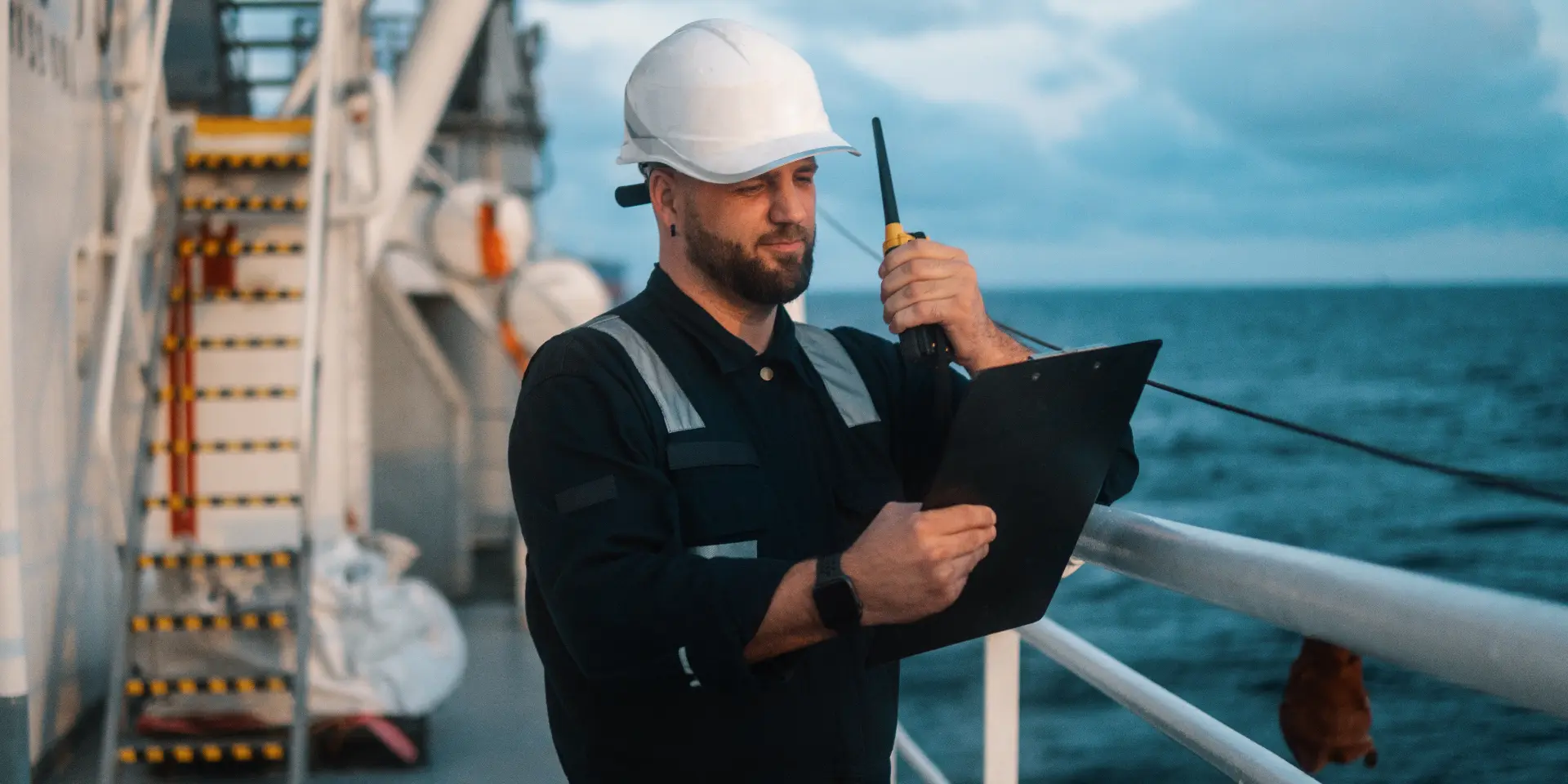 Marine officer recording operational checks on deck with a handheld radio.