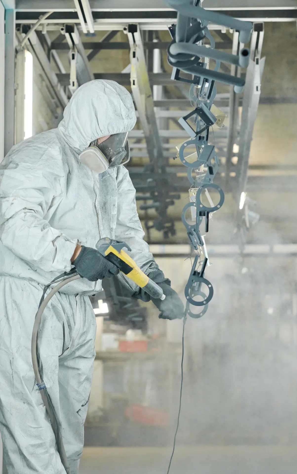 Coating specialist in full protective equipment spray-applying a finish to metal components in a controlled booth.