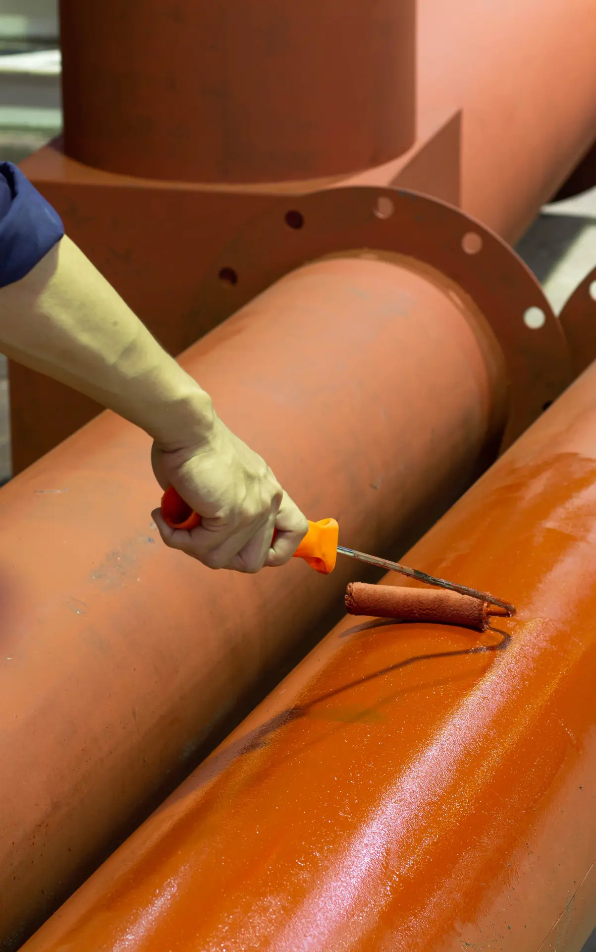 Close-up of a protective coating being roller-applied to prepared industrial pipework.